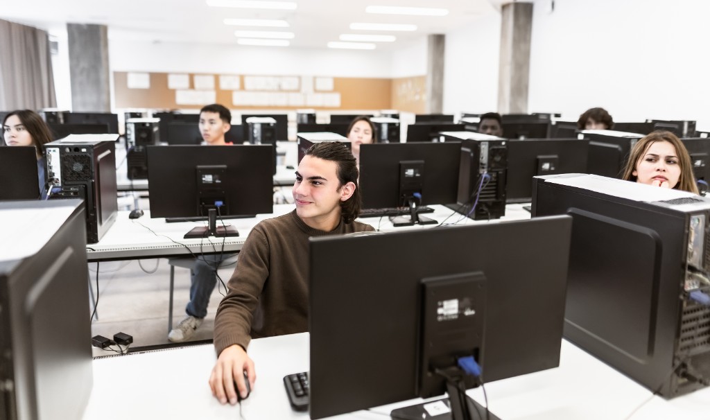 Students working at desktop computers in a bright, modern computer lab.